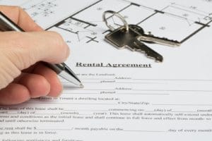 A people starts to fill out a a rental agreement. The floor plan and the keys from the apartment are in the background.
